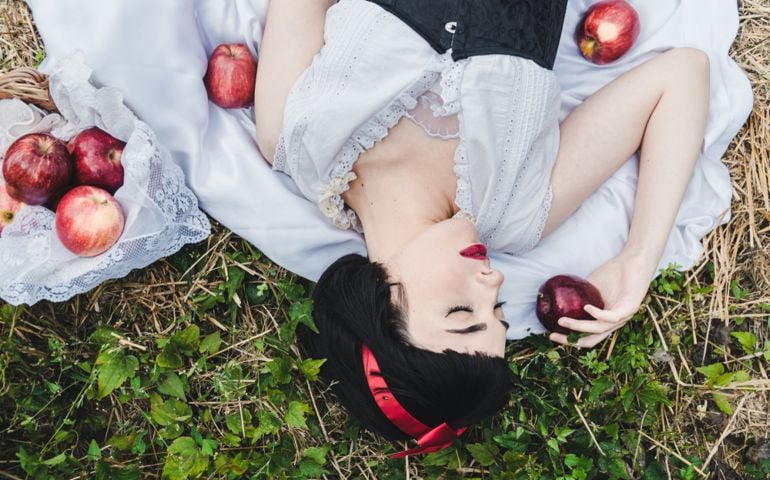 Snow White is laying in the floor in a deep sleep, surrounded by red apples.