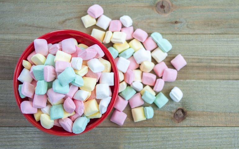 small red bowl overflowing with pastel butter mints on a wood background viewed from above