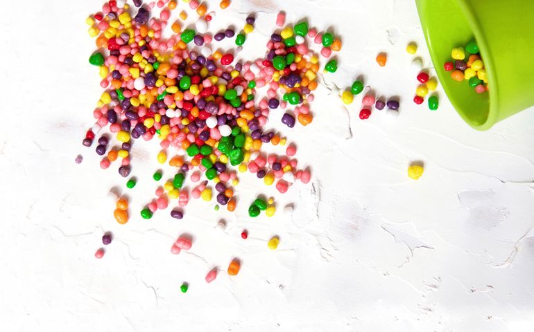 Rainbow colored candy pour out of the cup on a white background.