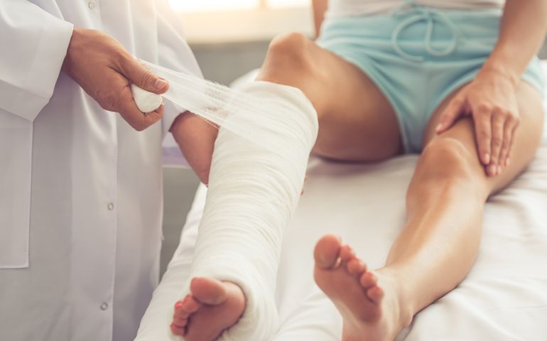 Cropped image of handsome doctor bandaging woman's broken leg while working in his office