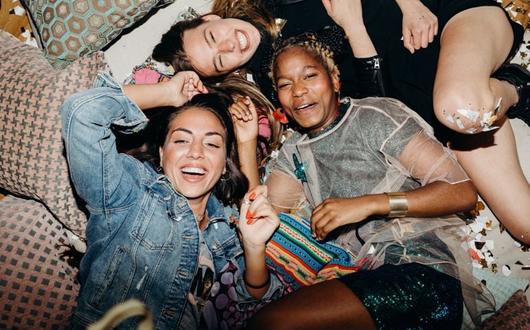 Happy smiling girlfriends relaxing on floor with cushions and confetti