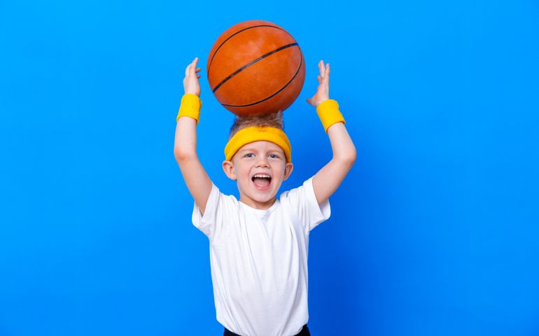 Sporty little boy with basketball ball over blue studio background. Gym workout. Child sportsman. Activity. Sport. Fitness, health and energy. Success.