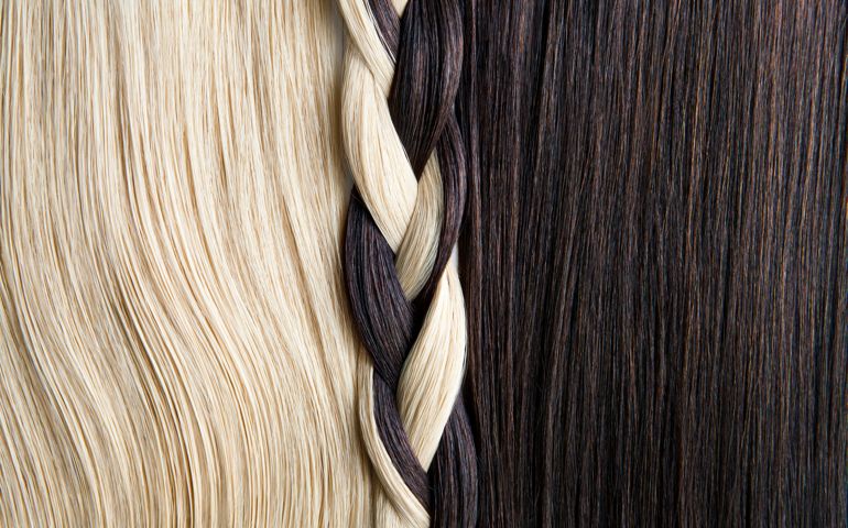Close up shot of straight blond and straight dark brown hair next to each other and braided together in the center.