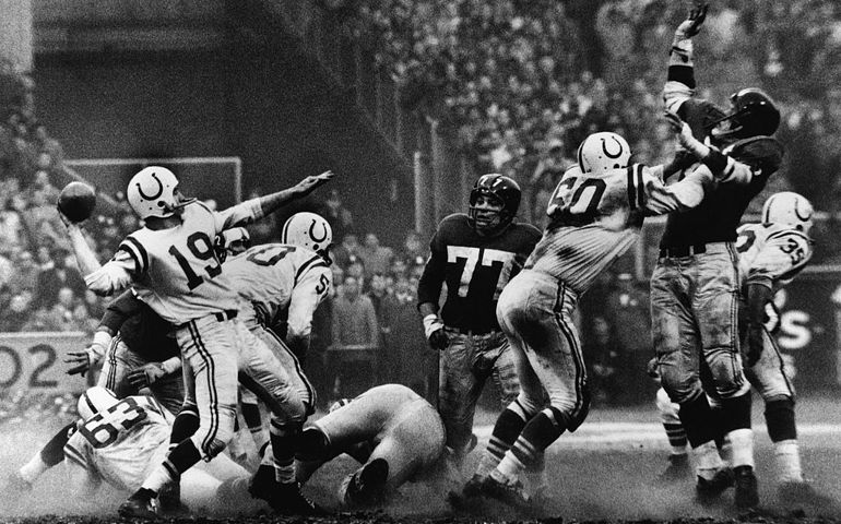 American quarterback Johnny Unitas #19 (1933 - 2002) (left) of the Baltimore Colts is about to throw a pass during a play in sudden death overtime of the NFL Championship game against the New York Giants, Yankee Stadium, New York, December 28, 1958. The Colts won 23 - 17. Other players visible include Art Spinney #63, Buzz Nutter #50, Dick Modzelewski #77, George Preas #60, Jim Katcavage #75 (1934 - 1995) (second from right), and Alan Ameche #35 (1933 - 1988).