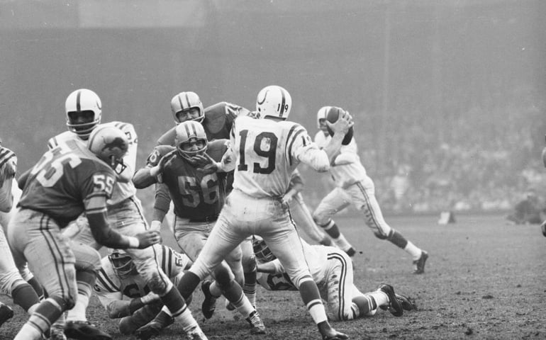 American professional football player Joe Schmidt #56 of the Detroit Lions charges towards Baltimore Colts quarterback Johnny Unitas #19 (1933 - 2002) during a game, Detroit, November 22, 1962. The Lions won 26 - 14.