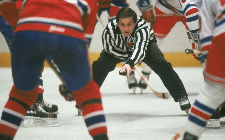 Canadian ice hockey linesman Ray Scapinello prepares to drop the puck during a face-off between the Montreal Canadiens and the New York Rangers at Madison Square Garden, New York, New York, 1980s.