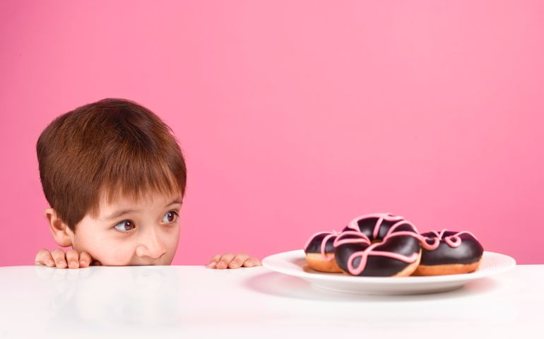 Young boy peering at a plate of doughnuts