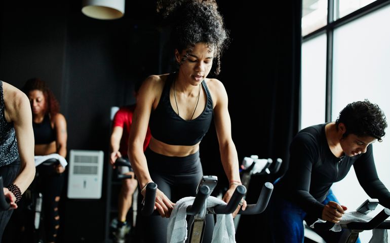 Woman riding out of saddle during indoor cycling class in fitness studio