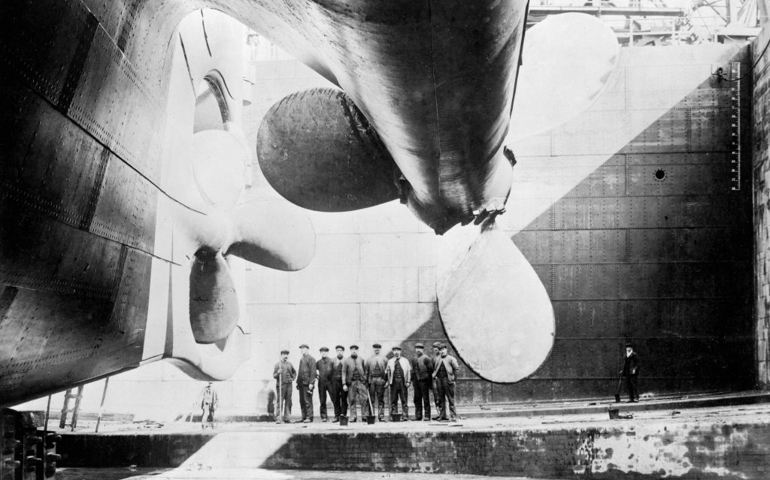 Workmen standing under one of the propellors of the Titanic, 31 May, 1911 b/w photo. (