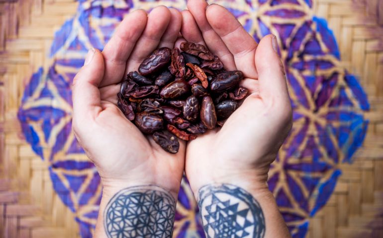 Hands with sacred geometry tattoos, holding cacao beans