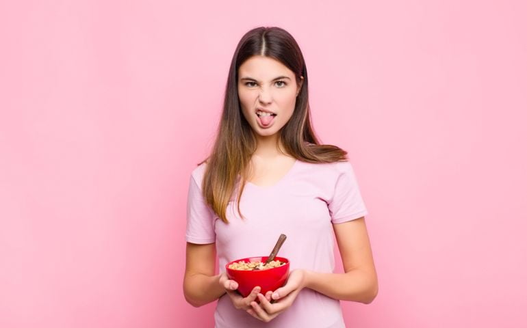 young pretty woman feeling disgusted and irritated, sticking tongue out, disliking something nasty and yucky with a breakfast bowl