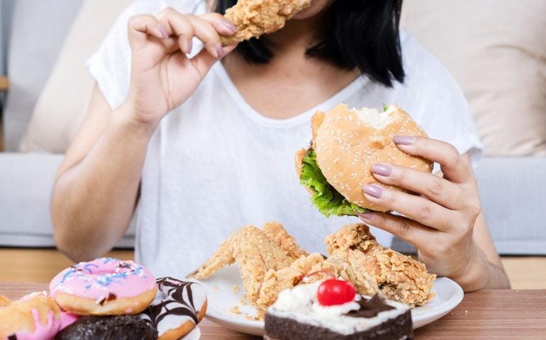 Binge eating disorder concept with woman eating fast food burger, fired chicken , donuts and desserts