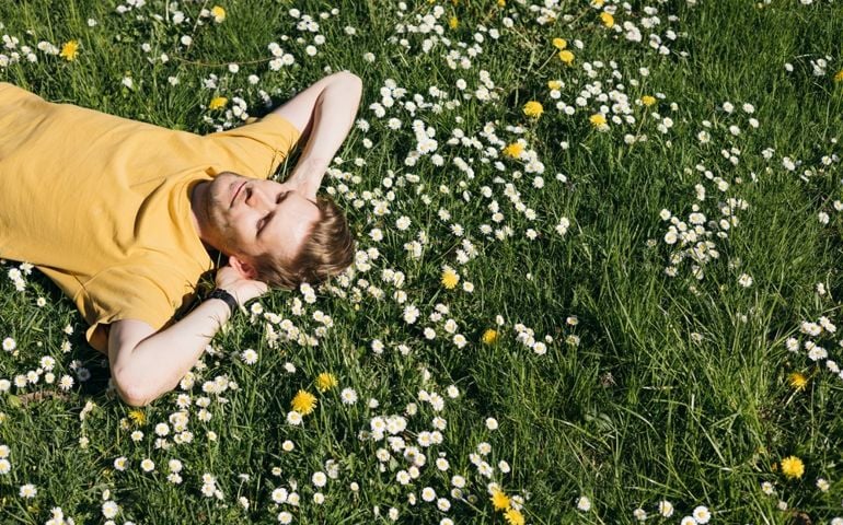 Young man laying in green grass with flowers