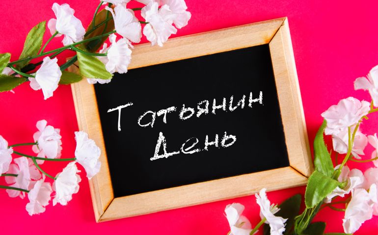 The inscription in Russian: Tatyanin day. Russian holiday on student's day. A chalk plaque surrounded by white flowers on a pink background