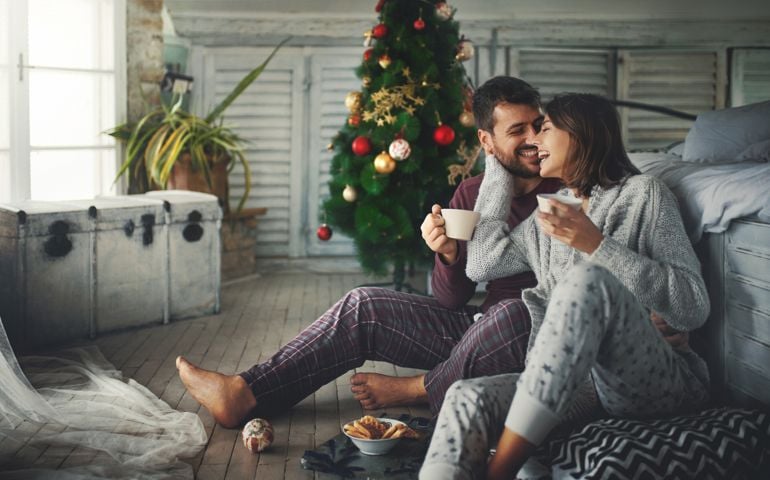 Closeup of a mid 20's couple having some coffee and relaxing by a window on a Christmas morning. They are laughing and captured in a very spontaneous moment.