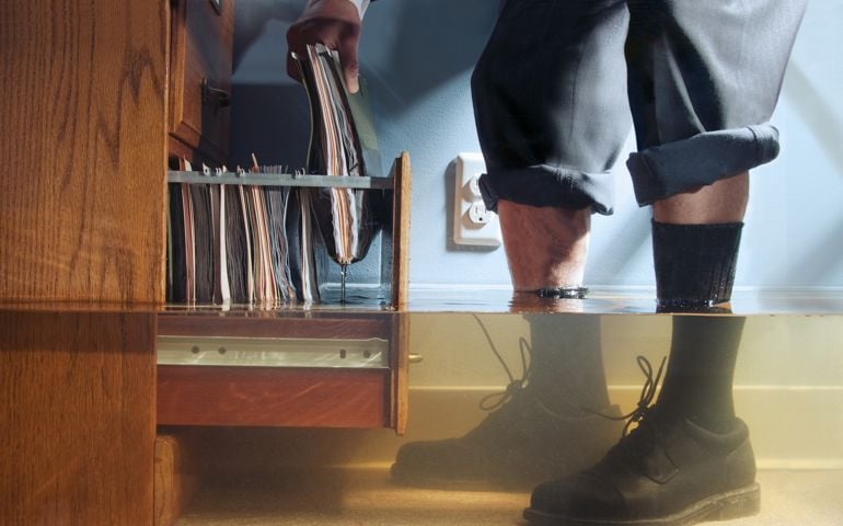 Businessman pulling files out of cabinet in flooded office, low angle