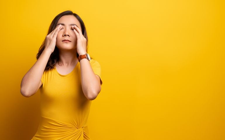 Woman has eyes pain isolated over yellow background