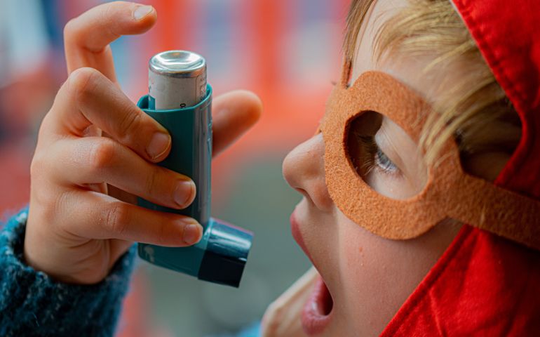 Young boy wearing a red pilot cap and aviator glasses using asthma inhaler for allergy.