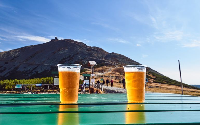 Plastic beer mugs with beer on the table against the background of the Sniezka mountain peak in Poland