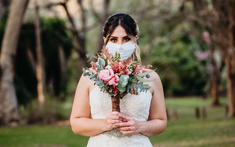 Bride with face protection mask holds bouquet with hands