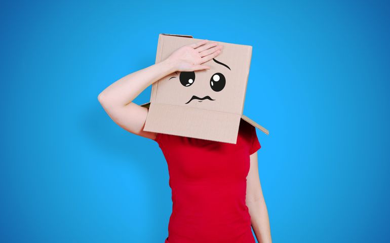 Person with cardboard box on its head with a dizzy face expression putting one hand in front of the face on deep blue background