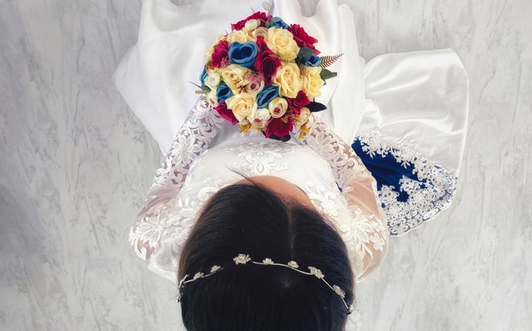 Upper view of a bride standing up, holding her bouquet, before her wedding. Her dress is white with blue details in it, matching the colours of the flowers on her bouquet.