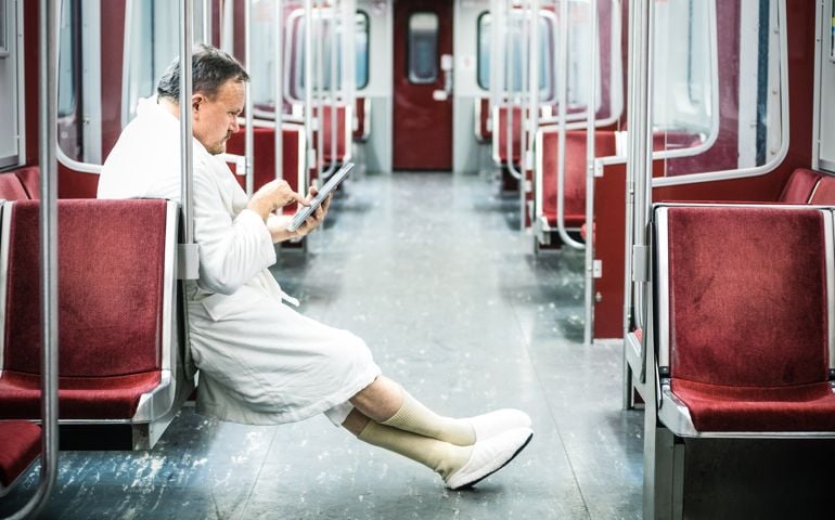Early commuter wearing bathrobe, slippers and browsing digital tablet on the underground train.