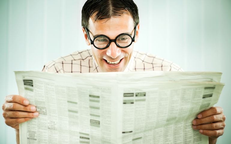 Funny looking nerd is smiling and reading the newspaper.
