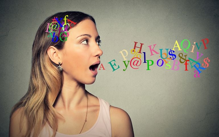 Side view portrait woman talking with alphabet letters in her head and coming out of her open mouth isolated grey wall background. Human face expressions, emotions. Communication, intelligence concept