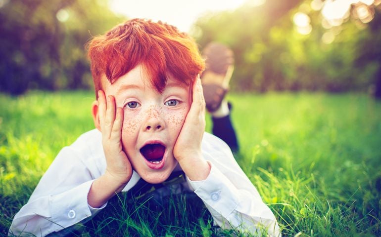 Surprised child with red hair and freckles in park in summer
