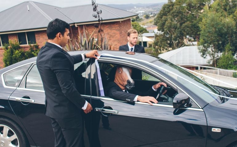 Groom and Groomsman getting car ready for wedding while driver has fun wearing a horse mask