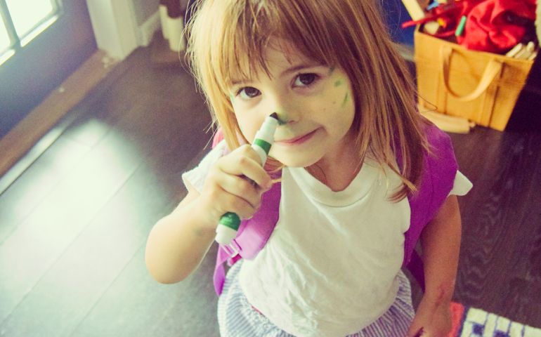 Little girl draws on her face with a marker