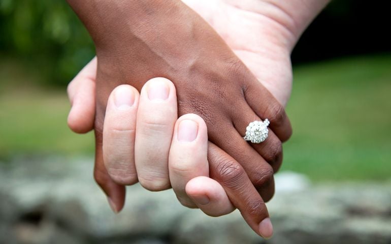 Interracial Couple Holding Hands and Diamond Engagement Ring, Close-Up