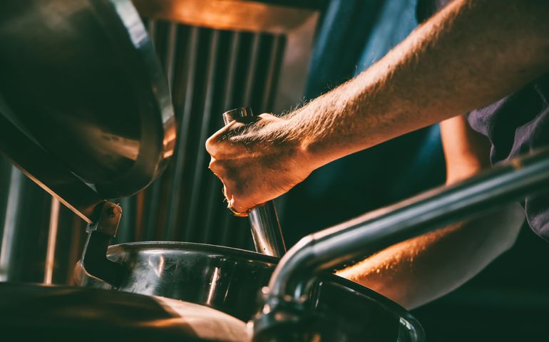One male worker checking the brew from a machine.