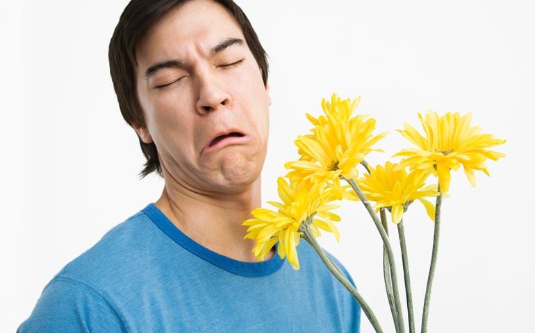 Asian young man holding bouquet of yellow gerber daisies with bad look on his face.