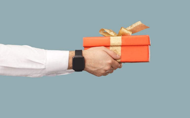 Business people concept, richly and success. human hand in white shirt with black smart watches holding red gift box with gold ribbon. profile side view. Indoor, studio shot on light blue background