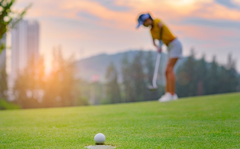 golf ball run through almost success drop to hole on the green with exciting watching by woman golf player in background