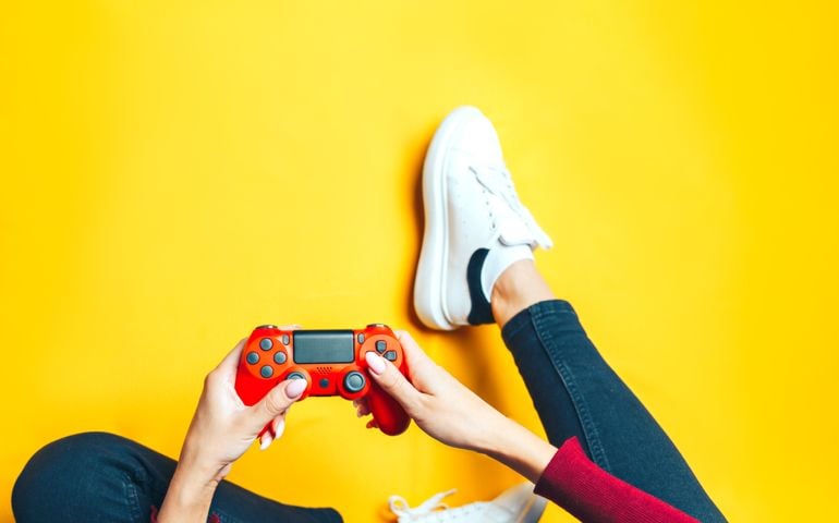 Young thin woman playing with red gamepad, sitting on yellow background. flat lay.