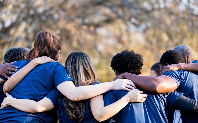 Diverse group of friends cleanup a park during a charity event. They are standing with their arms around one another.