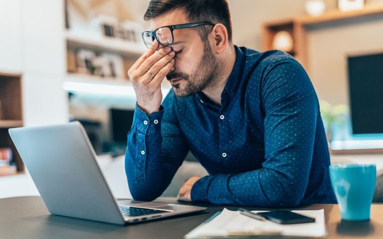 Tired young businessman working at home using lap top and looking Anxious