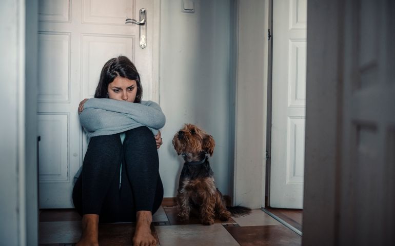 Woman with mental health problems is sitting desperate on the floor and crying and her dog is next to her