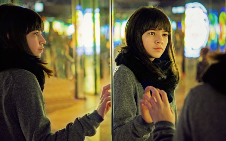 Depressed young girl is looking herself in a mirror