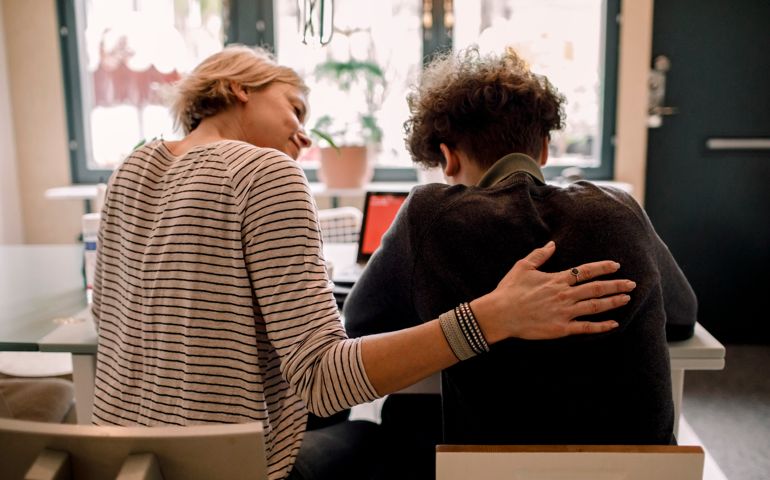 Mother sitting by teenage son studying at home