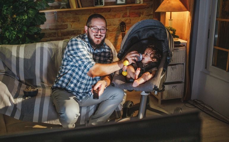 father watching tv with his young baby boy