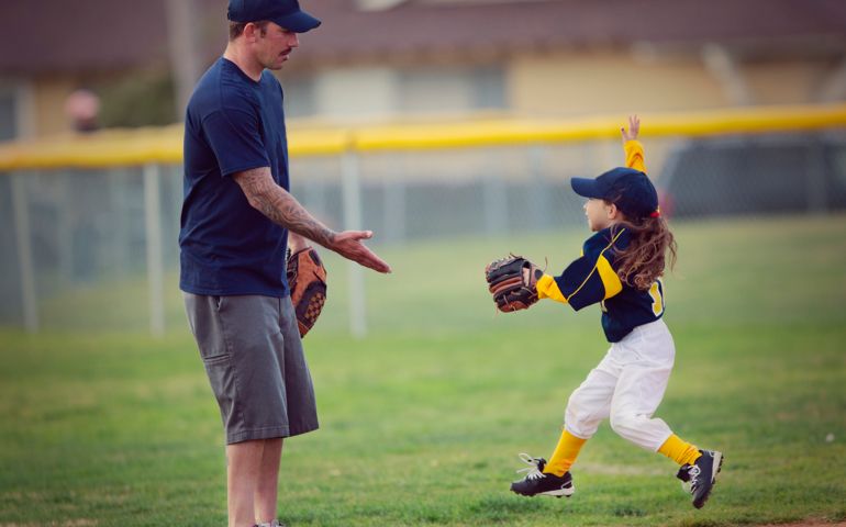Five year old girl running and giving her dad, one of the t-ball coaches a happy High Five with her hand