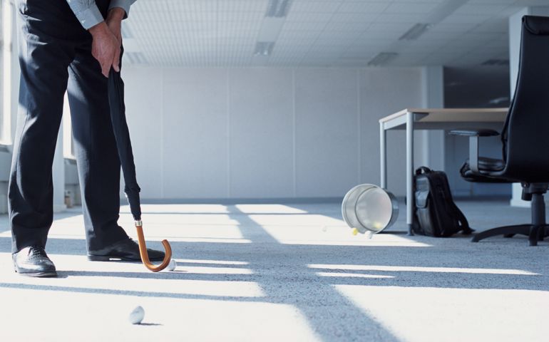 Businessman practicing putting with umbrella, in office, low section