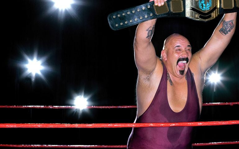 Male wrestler holding up championship belt in ring