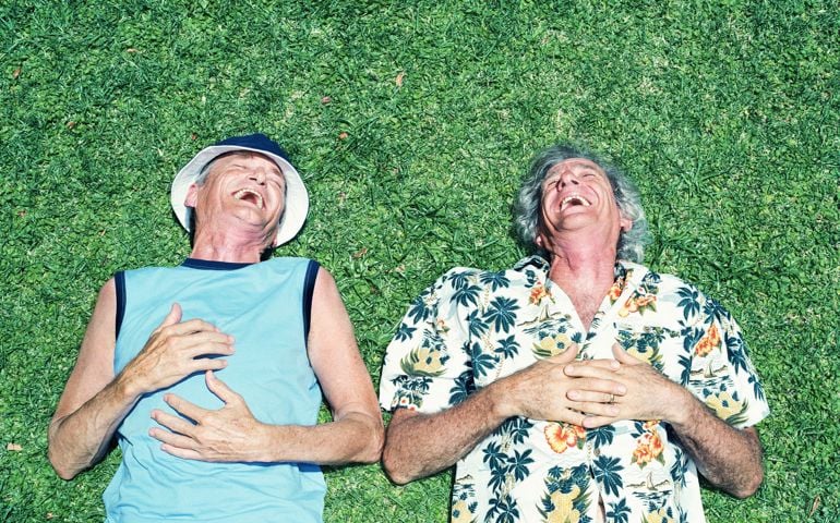 Two mature men lying on grass, laughing, overhead view