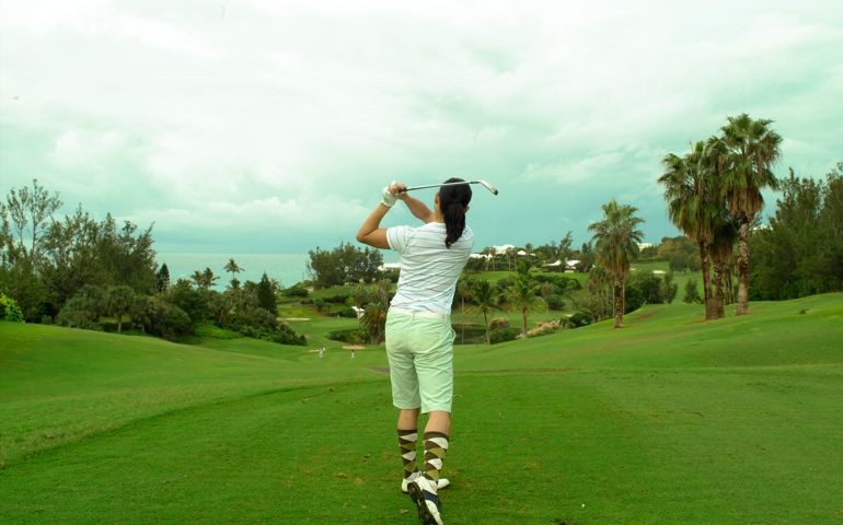 Young woman driving golf ball, rear view