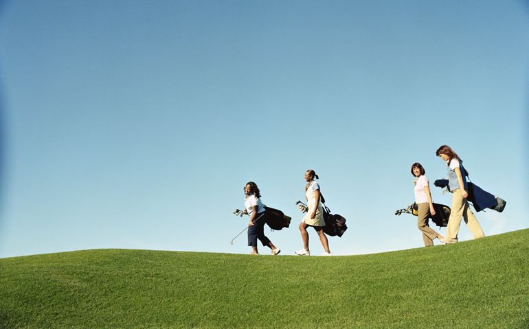 Female golfers carrying golf bags, side view